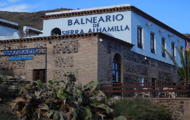 Edificio azul y blanco del Balneario de Sierra Alhamilla con chumberas en primer plano.